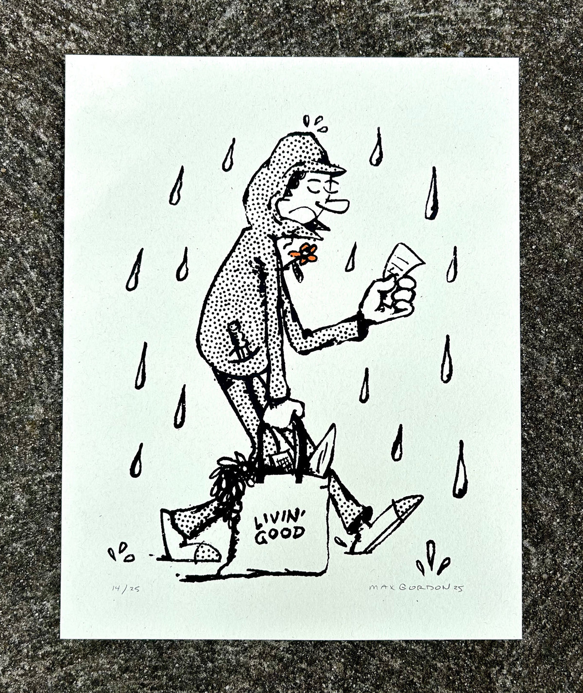 A black and white art print featuring a cartoon illustration of a man walking in the rain while holding a phone and a shopping bag labeled 'LIVIN' GOOD', displayed on a textured gray surface.