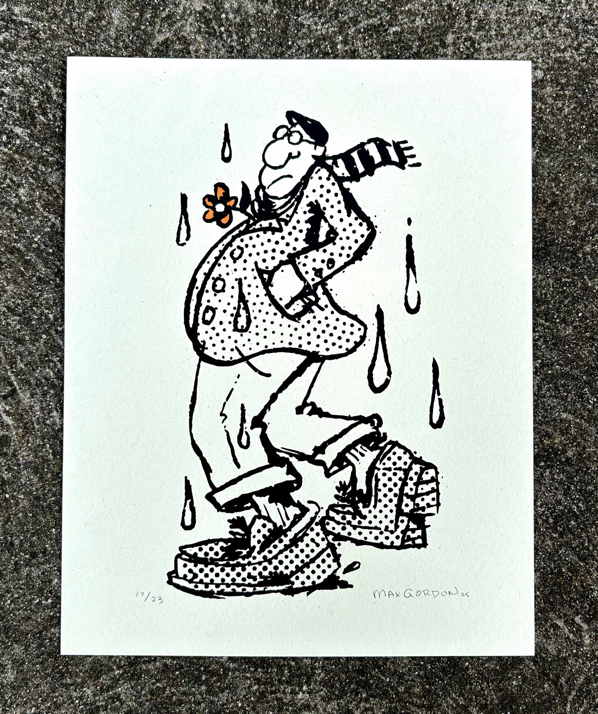 A black and white ink illustration print on white paper, depicting a cartoon figure with raindrops and a flower, photographed on a textured gray surface.