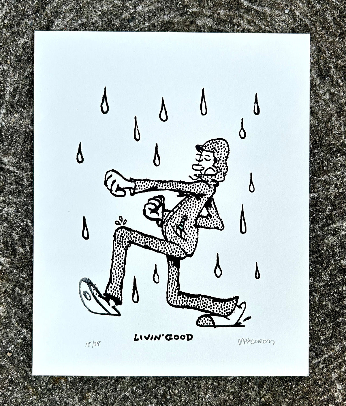 A white art print featuring a black hand-drawn illustration of a person kneeling and reaching upward under falling rain droplets, with the text 'Livin' Good' at the bottom, displayed on a textured gray stone surface.
