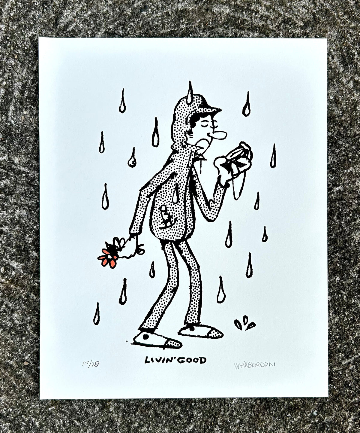 A white art print featuring a black-and-white cartoon figure walking in the rain while holding a flower, placed on a textured gray stone surface. The print has a signed and numbered edition mark at the bottom.