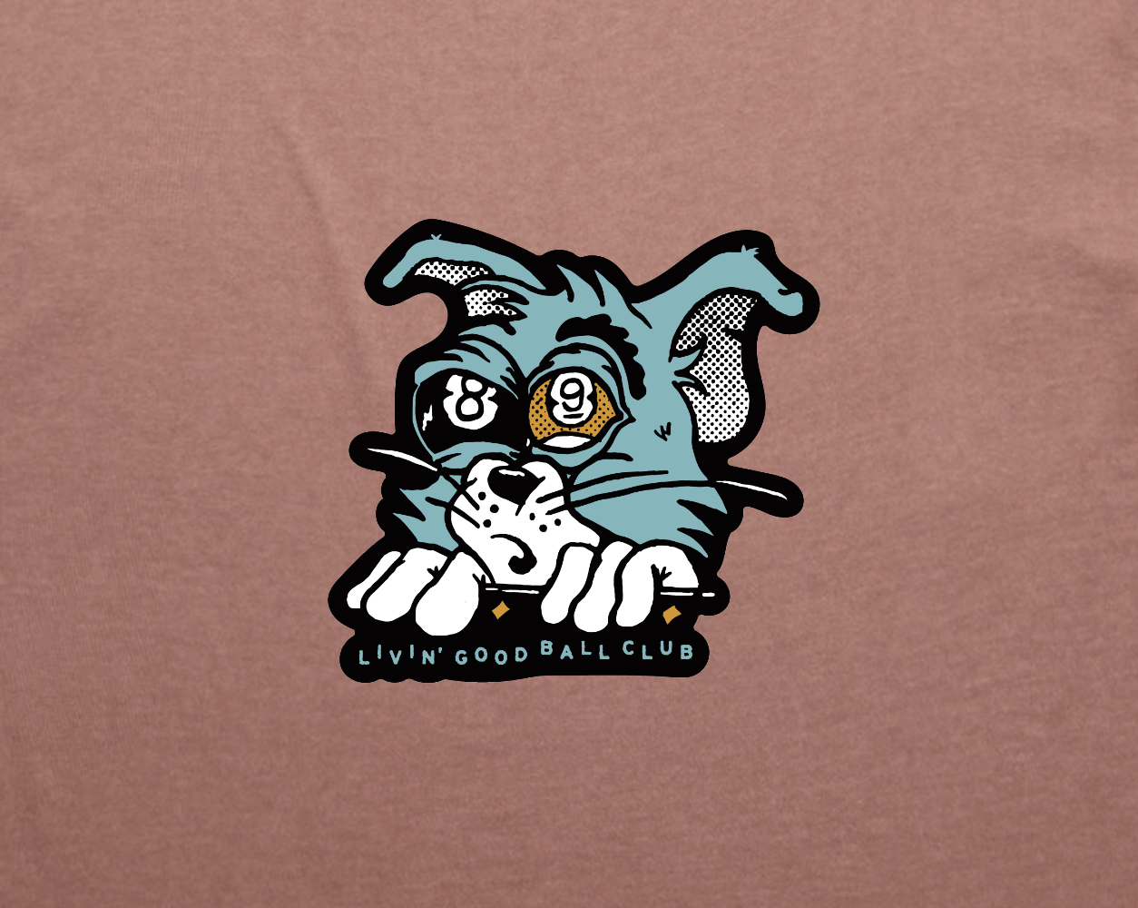 A close-up of a brown t-shirt featuring a graphic print of a cartoon cat peeking over a line with the text 'LIVIN' GOOD BALL CLUB' underneath.