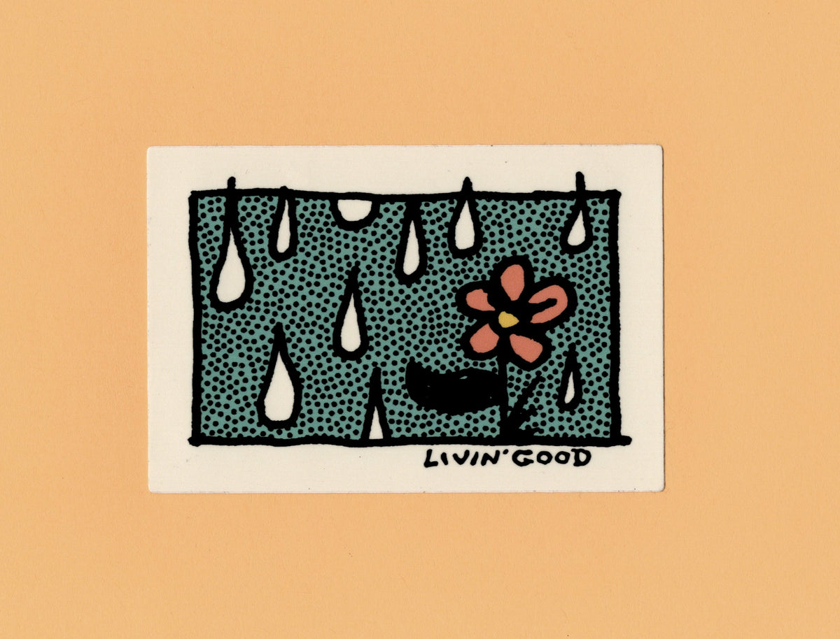 A square art print or card featuring a stylized illustration of raindrops falling over a dark teal ground with a pink flower and black outlines, centered on a warm peach background. The signature 'LIVIN' GOOD' appears at the bottom of the artwork.