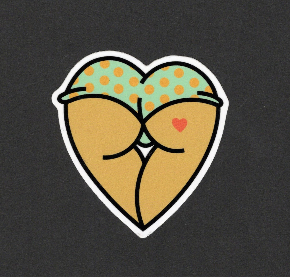 A heart-shaped sticker featuring a cartoon illustration of two censored faces kissing, with green polka-dot hats and a small red heart, shown on a dark charcoal background.