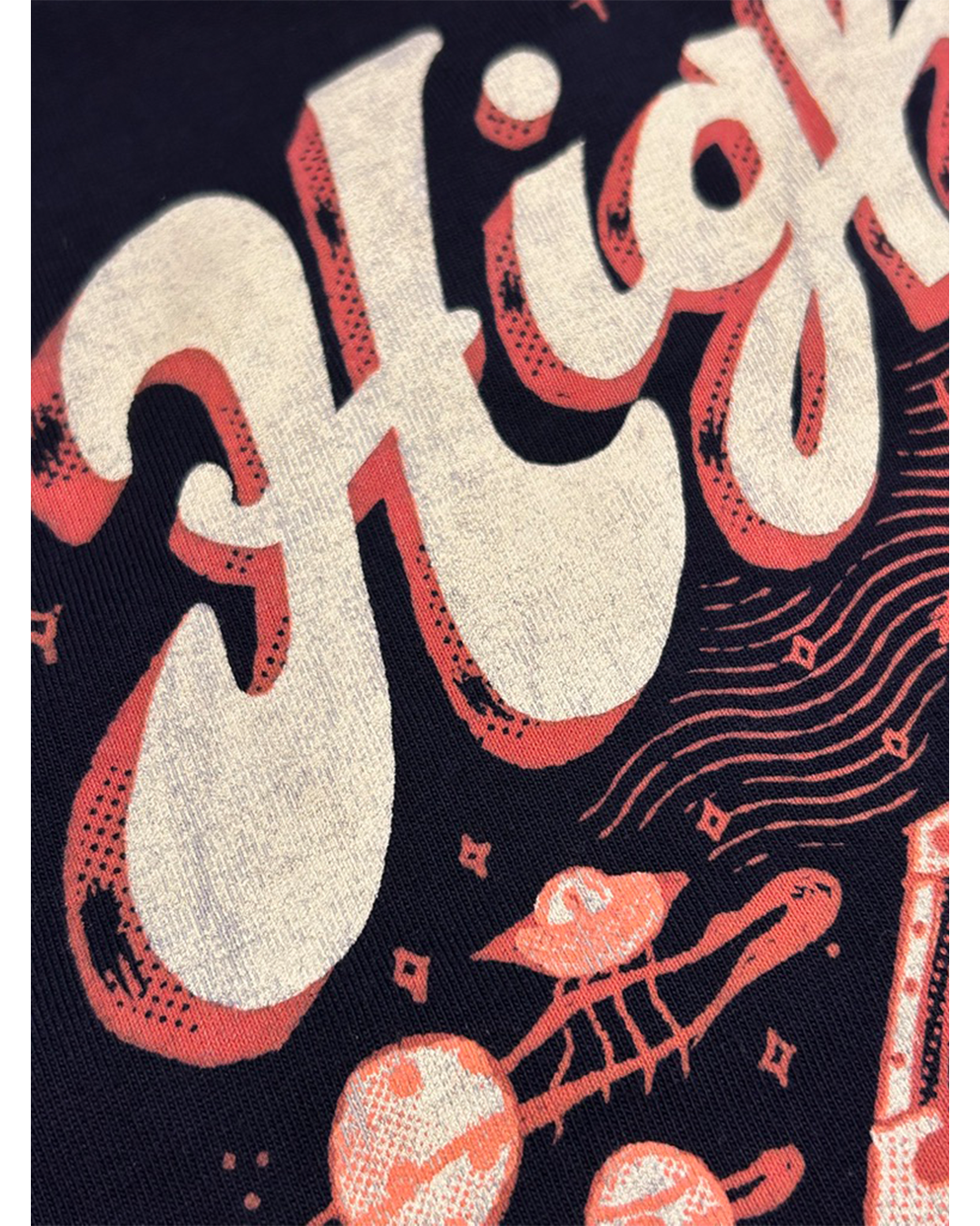 A close-up of a graphic print featuring bold retro-style cream lettering with coral-red drop shadows and halftone details on a dark navy background, alongside abstract wavy lines and small graphic elements.