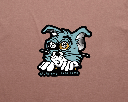 A close-up of a brown t-shirt featuring a graphic print of a cartoon cat peeking over a line with the text 'LIVIN' GOOD BALL CLUB' underneath.